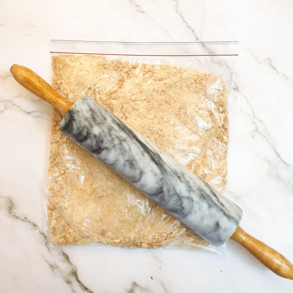 Biscuits crumbs in a plastic bag with a rolling pin.