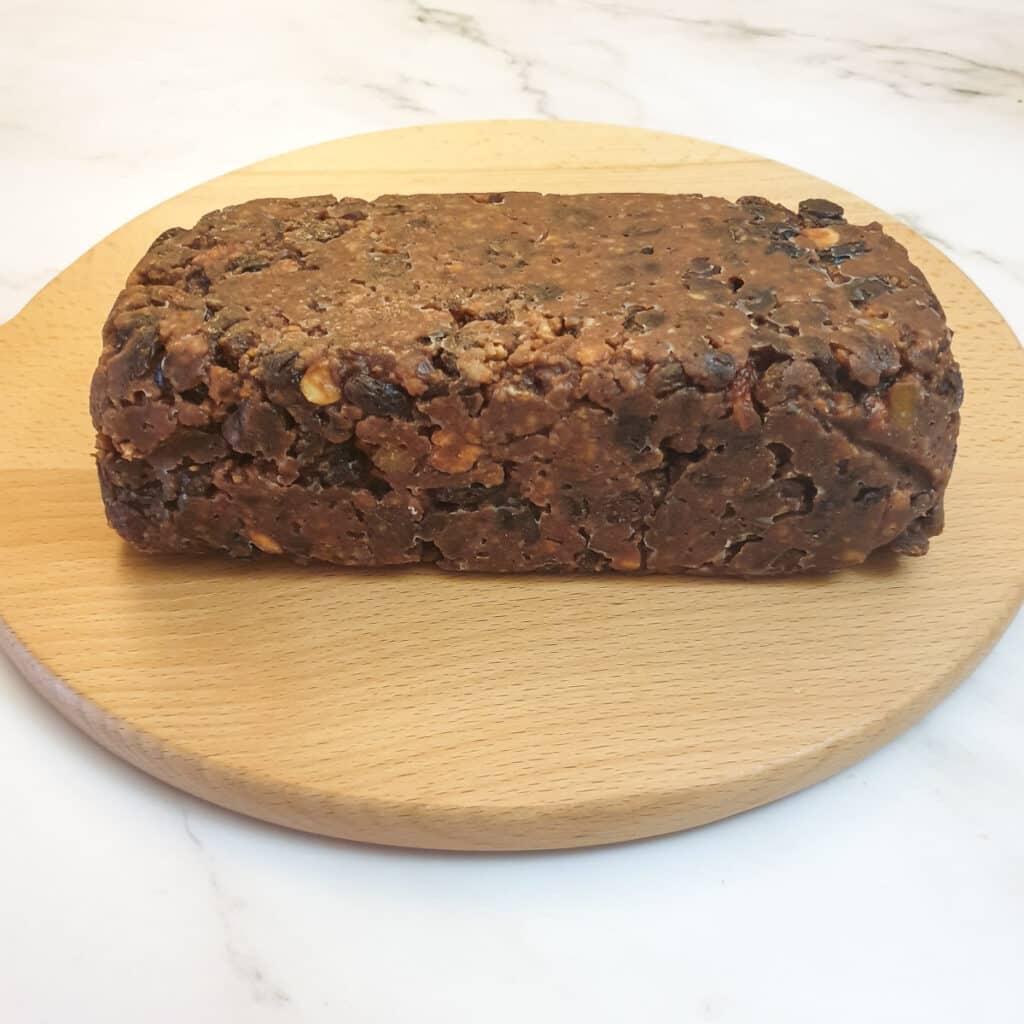 A no-baked Christmas cake out of the tin on a wooden plank.