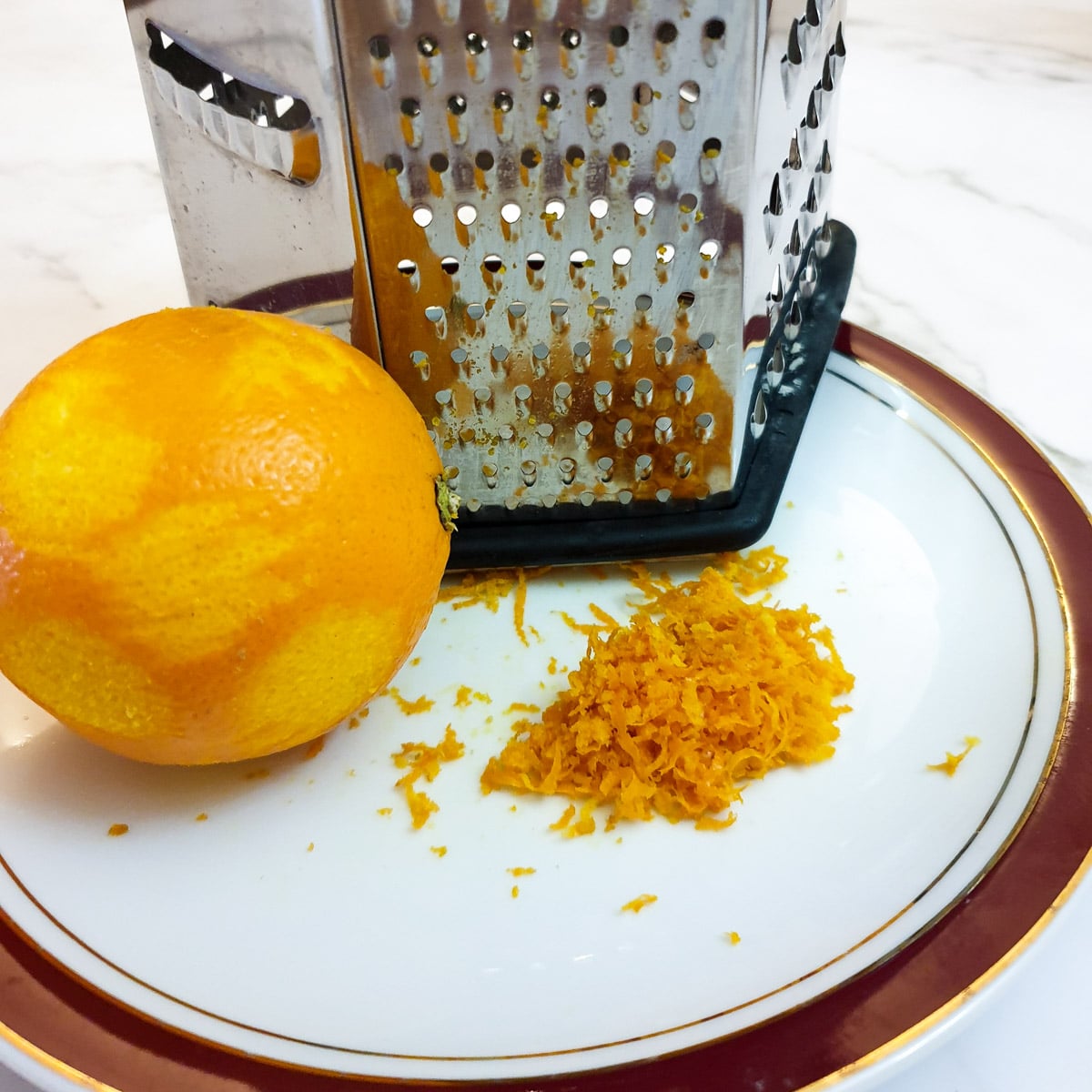An orange next to a grater with orange zest on a plate.