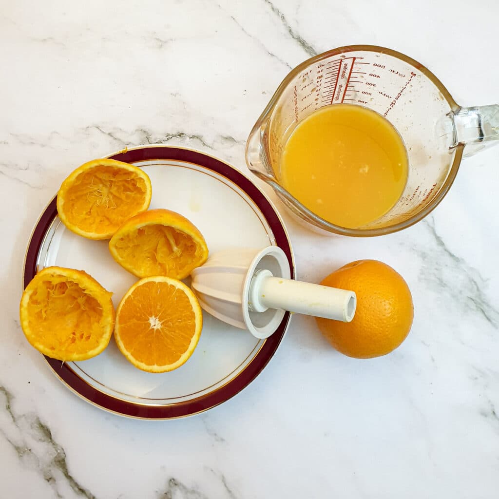 4 orange halves being juiced into a jug.