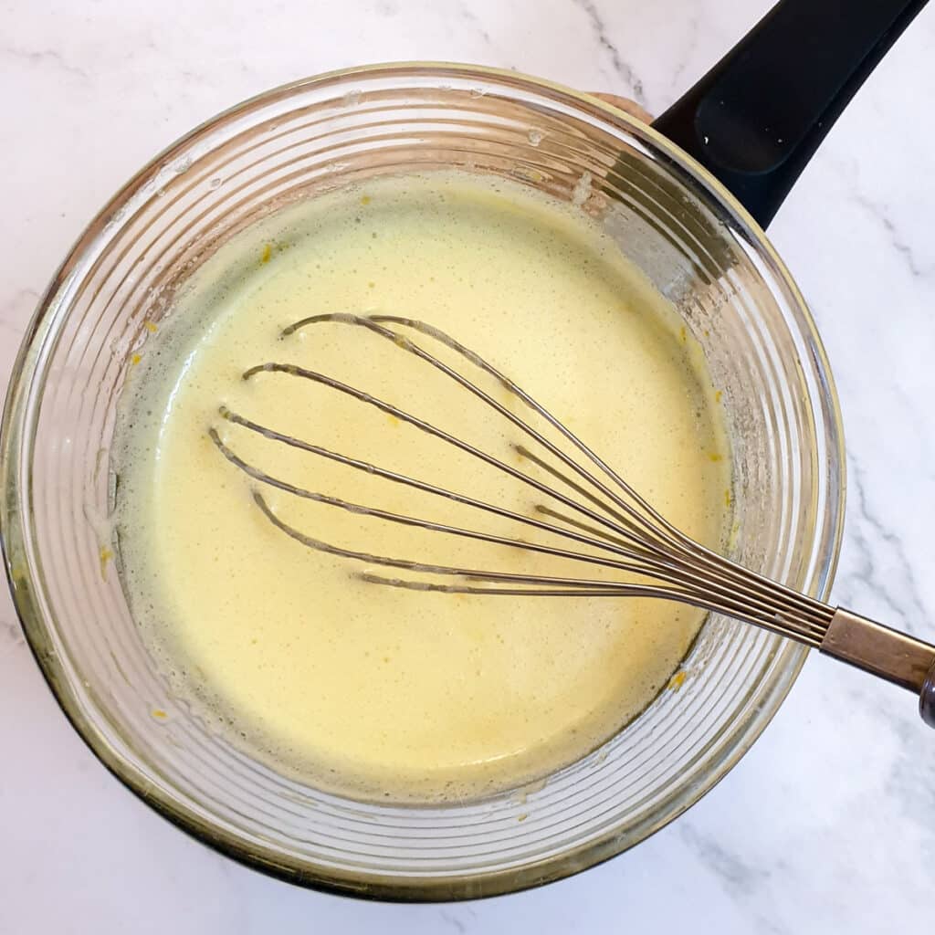 Ingredients for orange curd being whisked in a glass bowl.