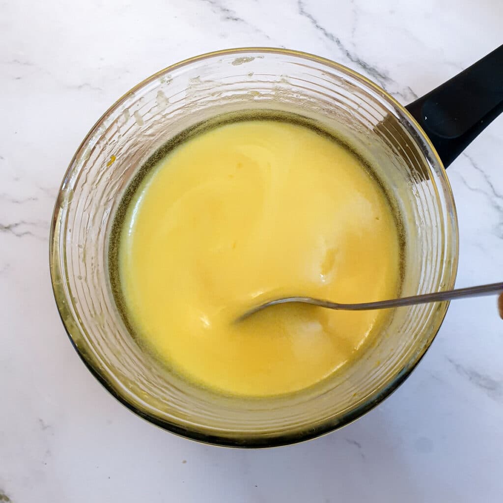 Orange curd in a glass bowl showing the consistency.
