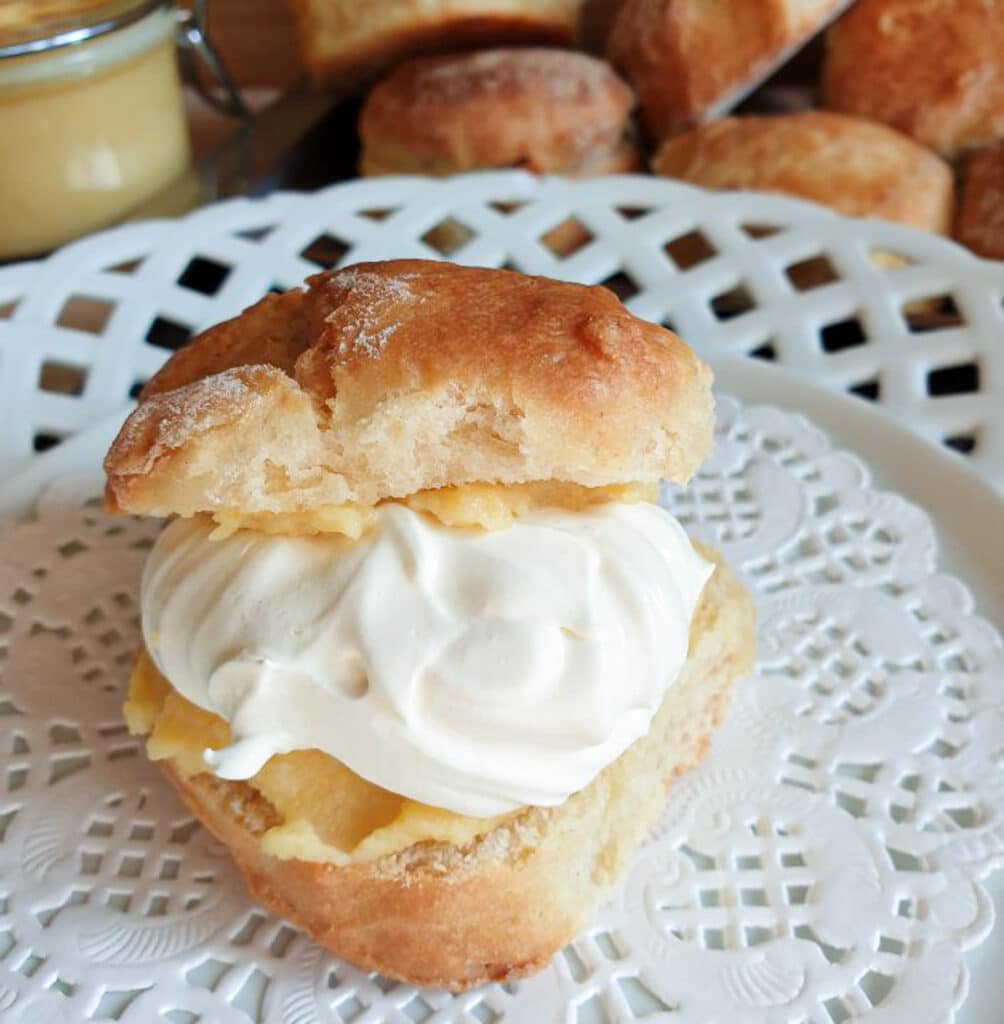 A scone filled with cream and orange curd on a white plate.