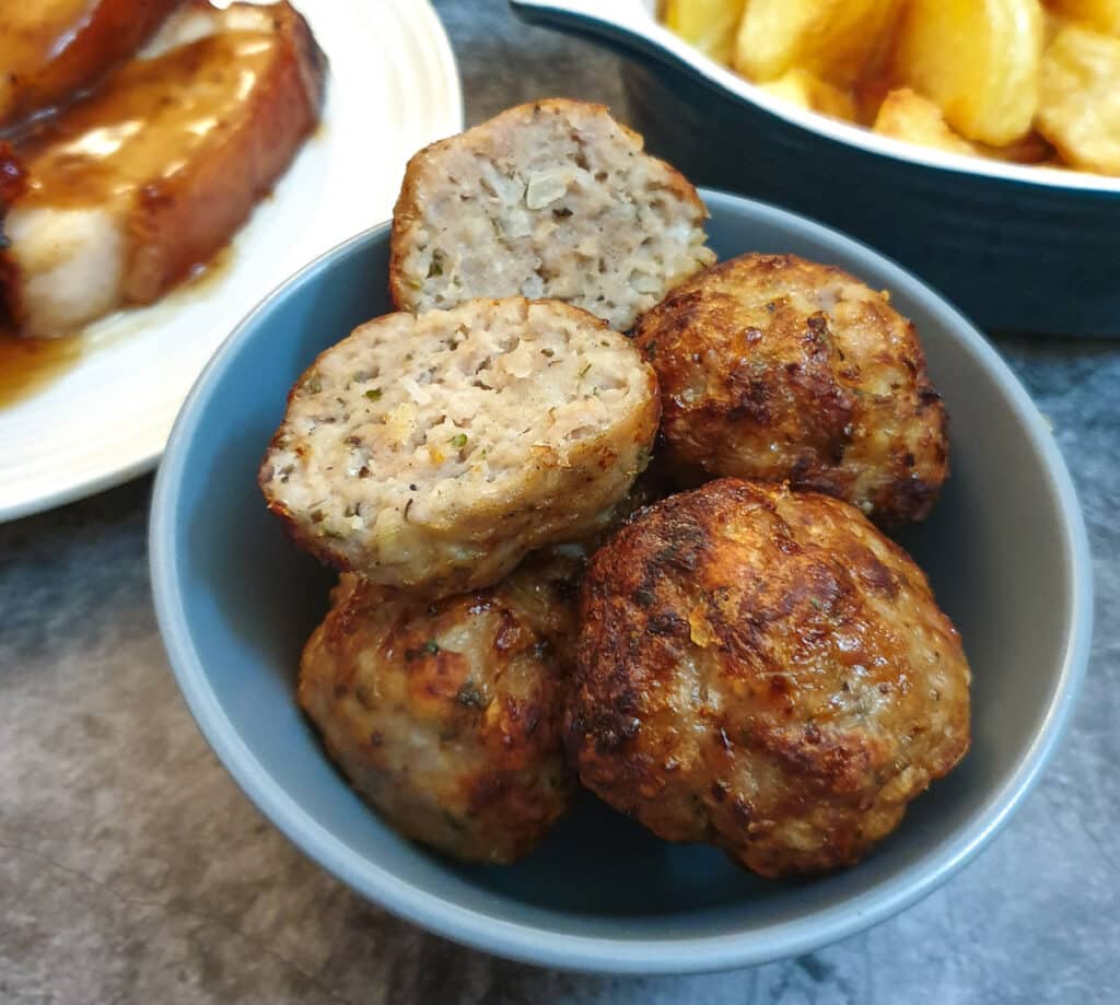 Sage and onion sausage stuffing balls in a dish with one cut in half to show the texture.