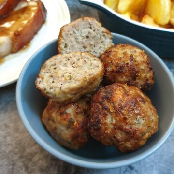 Sage and onion sausage stuffing balls in a dish with one cut in half to show the texture.