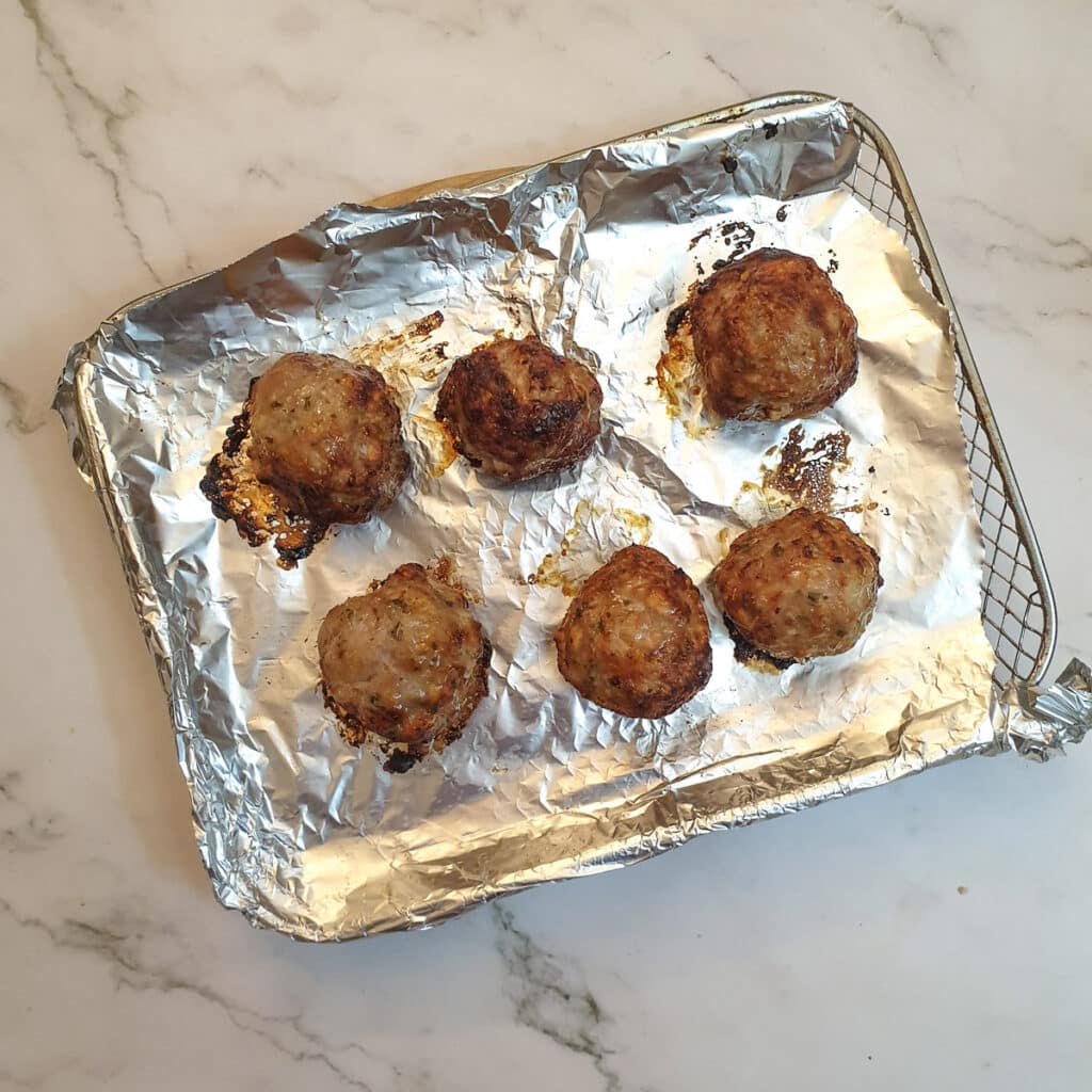 6 cooked stuffing balls on an air-fryer oven shelf.