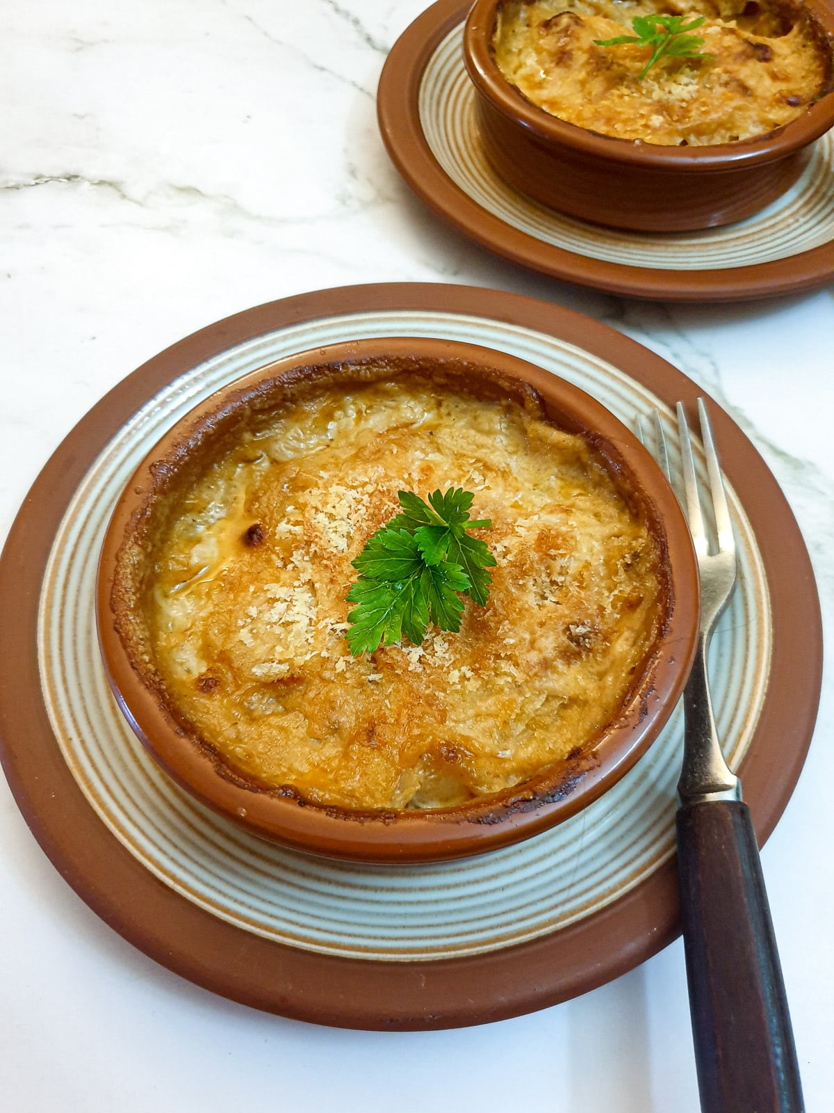 A prawn and scallop starter, covered with cheese and breadcrumbs, in a brown dish.