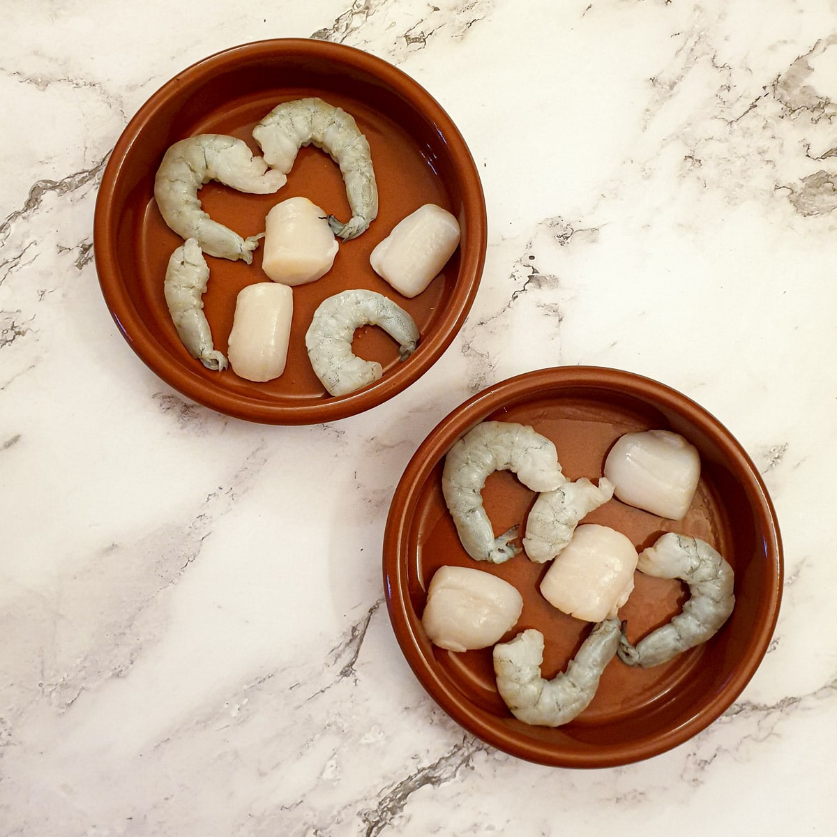 Raw prawns and scallops arranged in 2 ramekins.