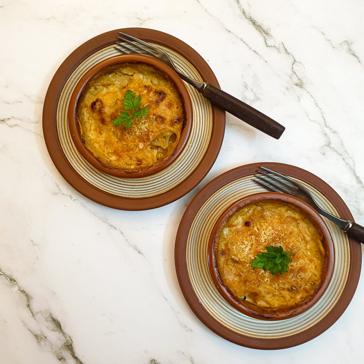 2 baked dishes of prawn and scallop au gratin garnished with a sprig of parsley.