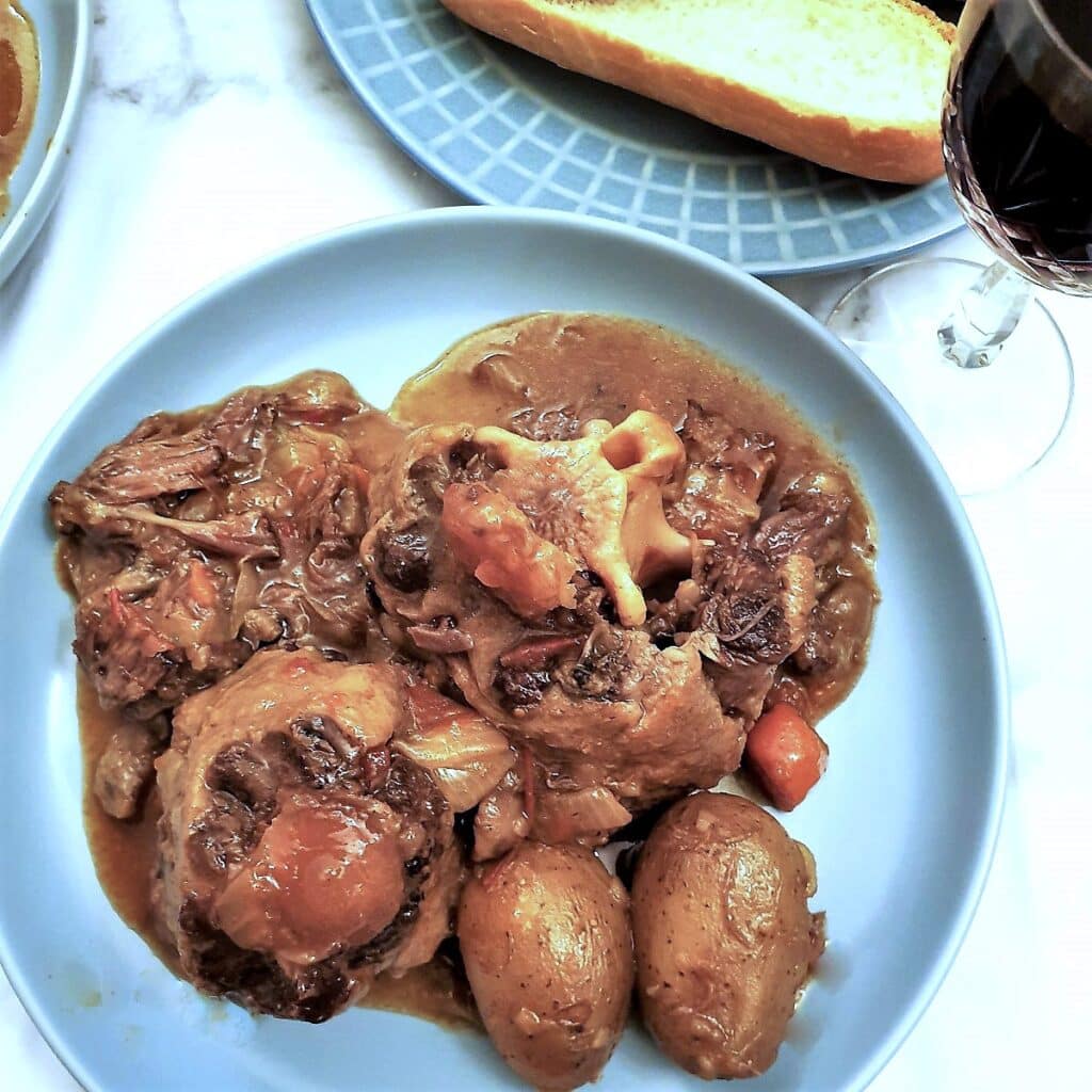 Slow cooker oxtail stew on a blue plate with potatoes.