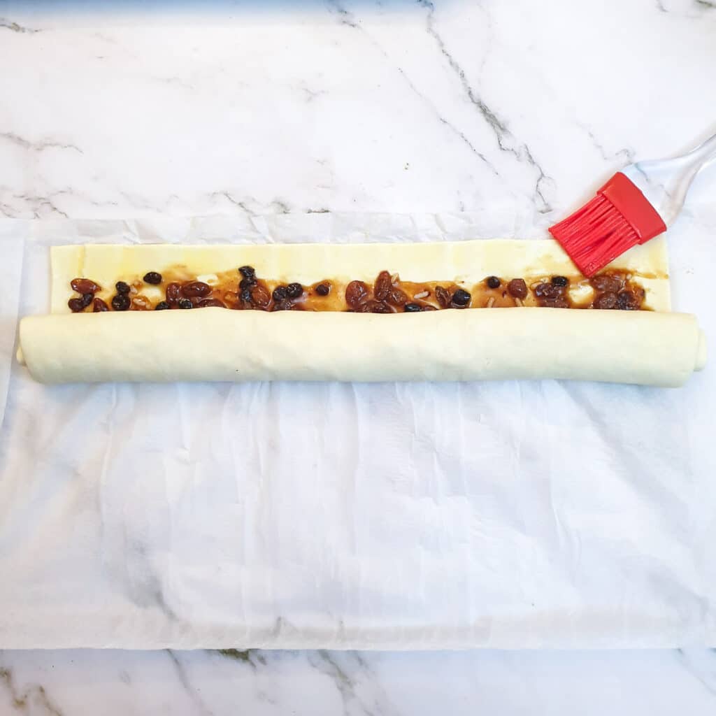 The edge of the rolled pastry being brushed with beaten egg.