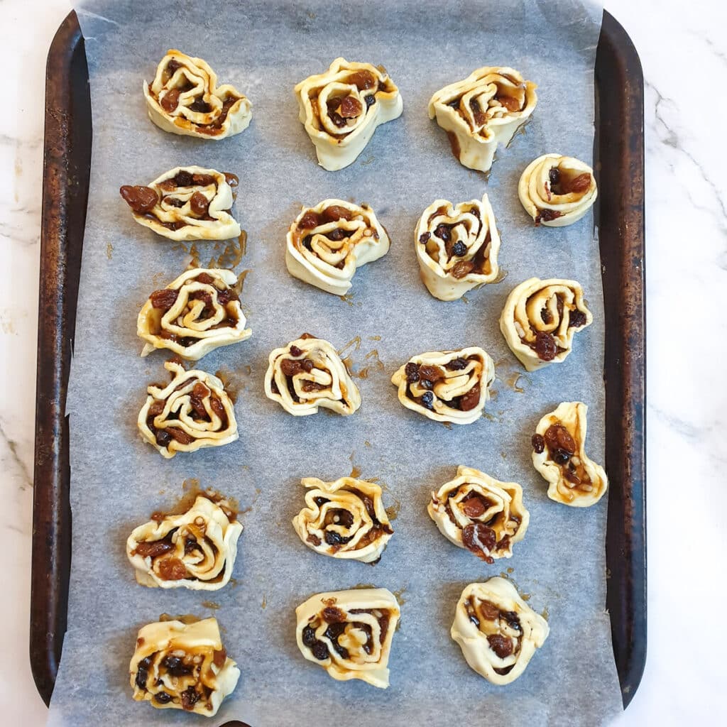 Unbaked Christmas fruit pinwheels on a baking tray.