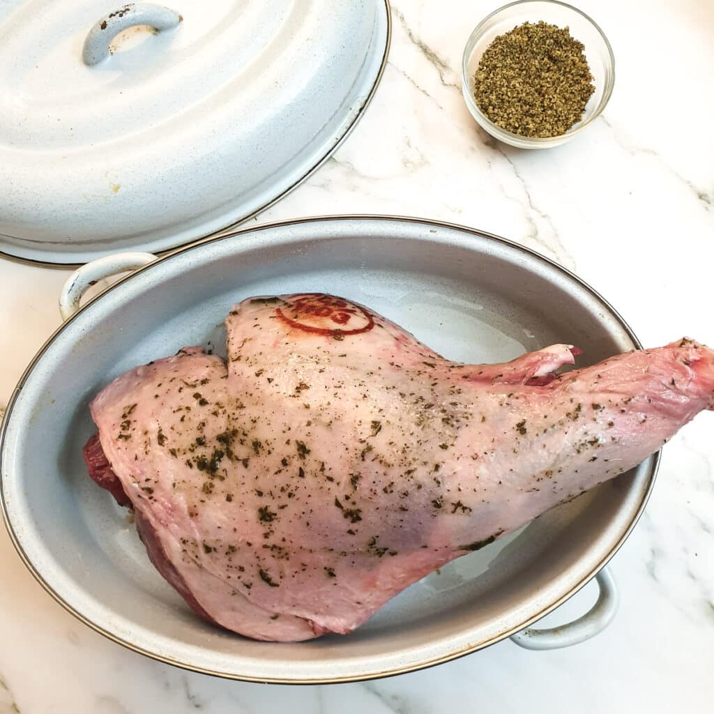 An uncooked leg of lamb rubbed with oil and mint sauce in a roasting pan.