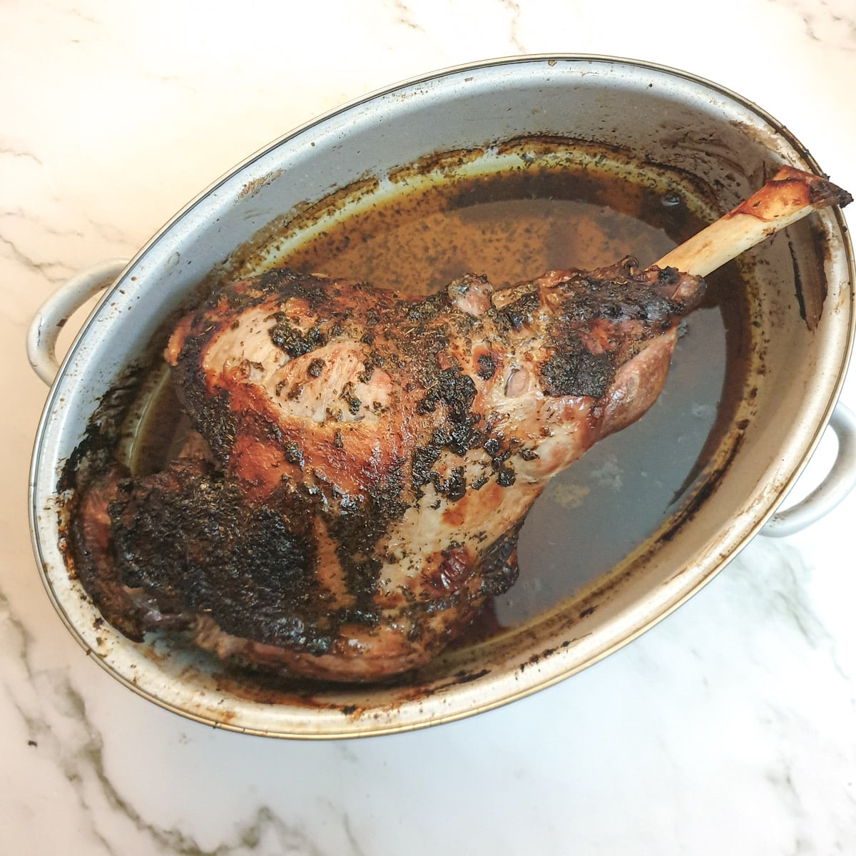 A cooked leg of lamb in a roasting pan.