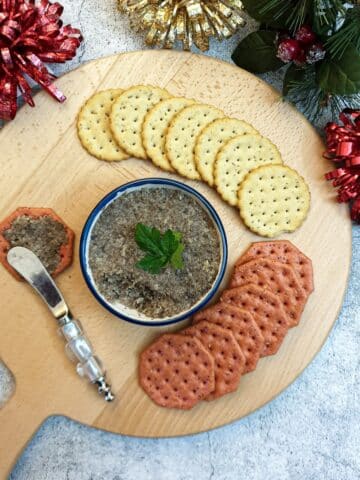 A dish of mushroom pate on a wooden board surrounded by crackers.