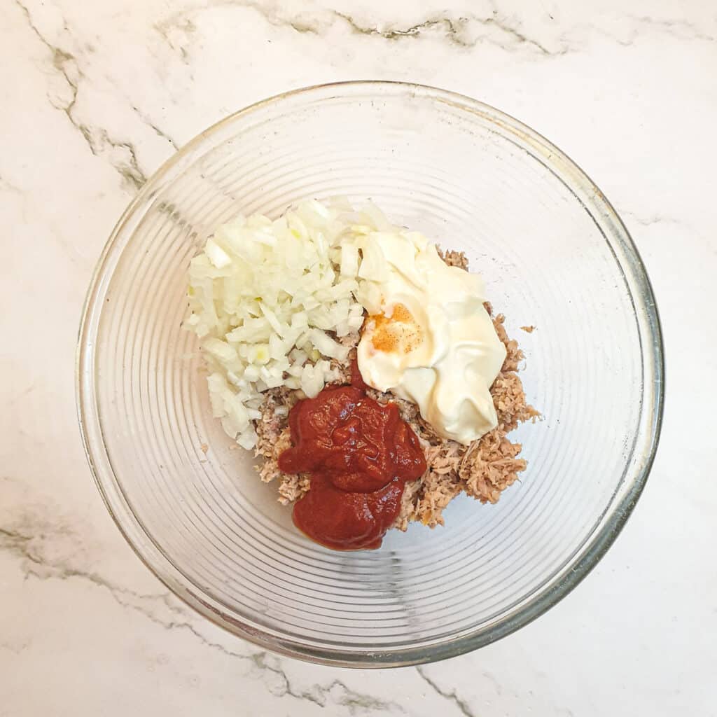 Tuna, mayonnaise, tomato ketchup and finely diced onions in a mixing bowl.