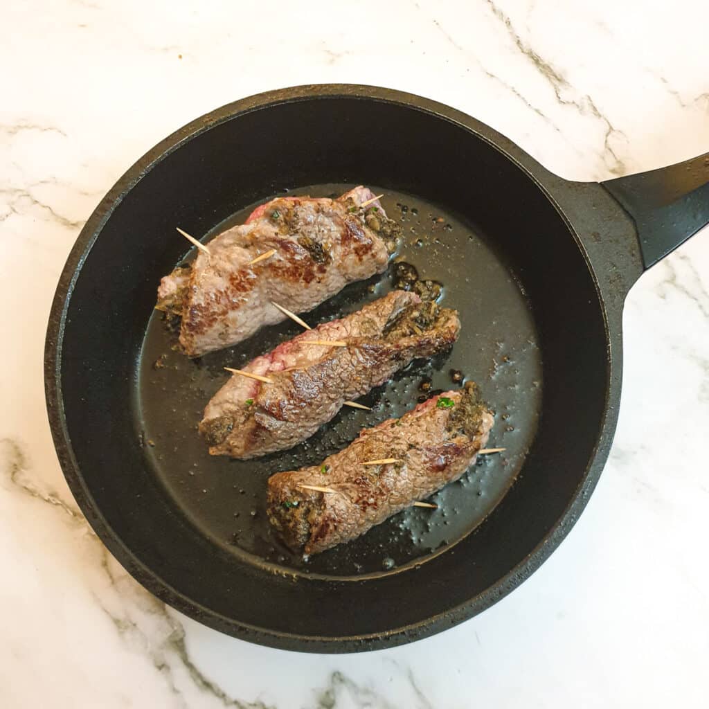 Three steak roulades frying in a frying pan.