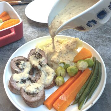 Steak roulade with mushroon stuffing on a plate with vegtables, with gravy being poured from a jug.