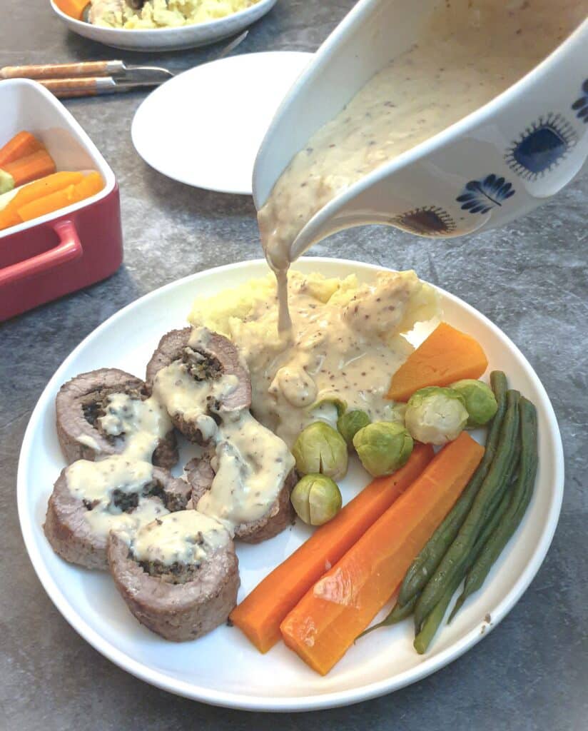 Steak roulade with mushroon stuffing on a plate with vegtables, with gravy being poured from a jug.