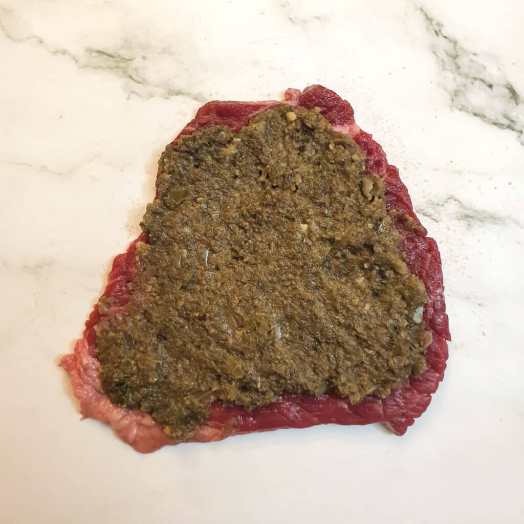 Mushroom mixture spread thinly onto a slice of steak.