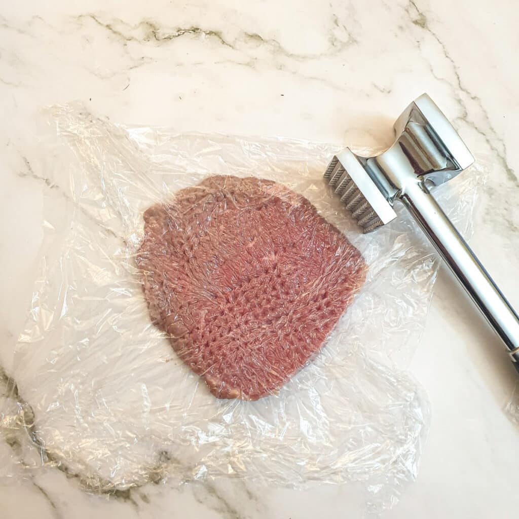 A slice of steak being thinned out with a meat mallet.