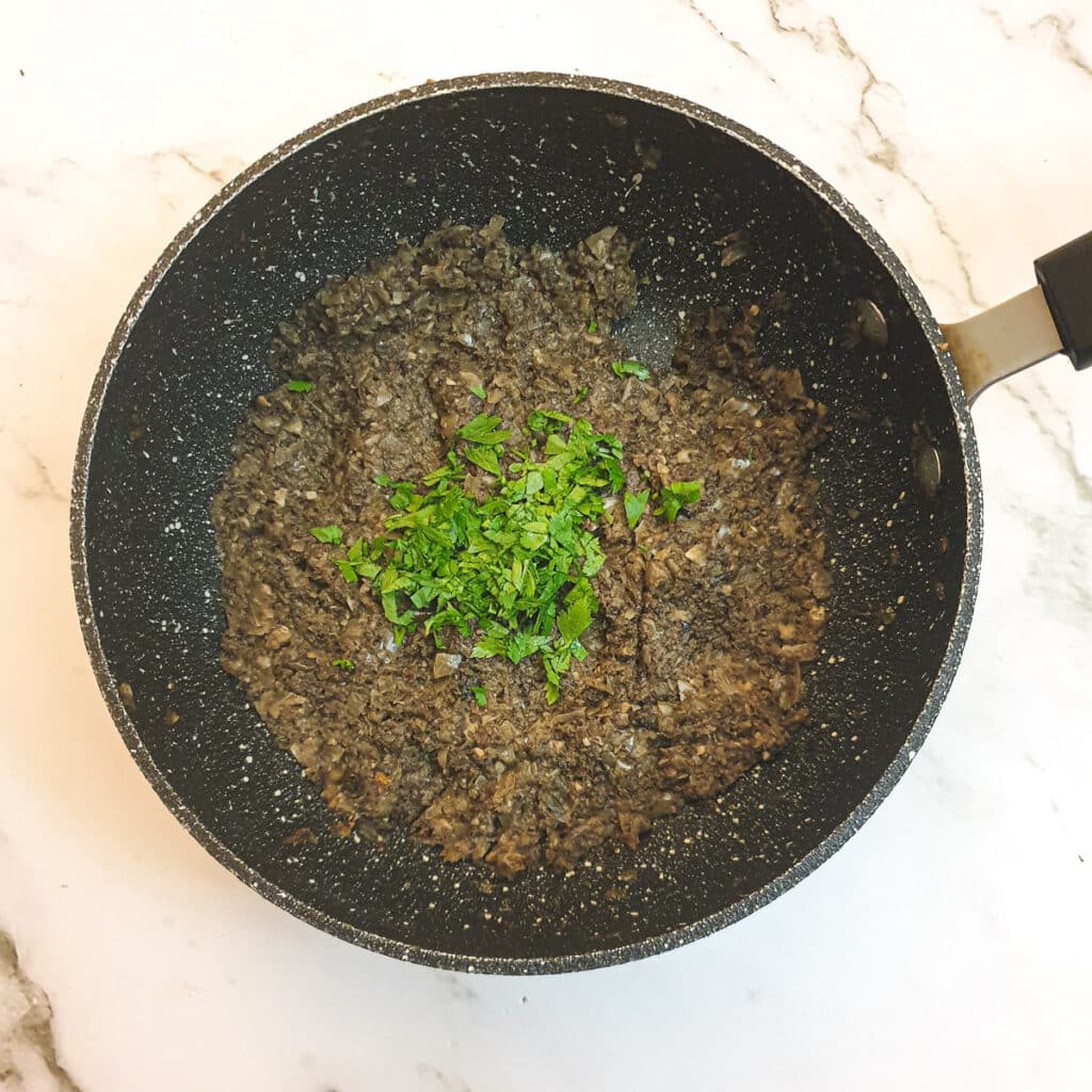 Chopped parsley being mixed with the mushroom mixture.