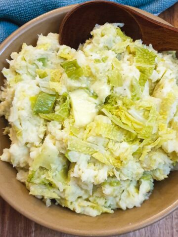 Irish colcannon in a brown serving dish with a brown wooden spoon.