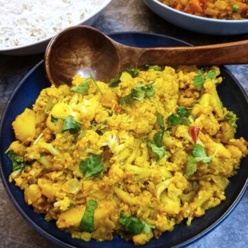 Aloo gobi in a serving dish with a wooden spoon.