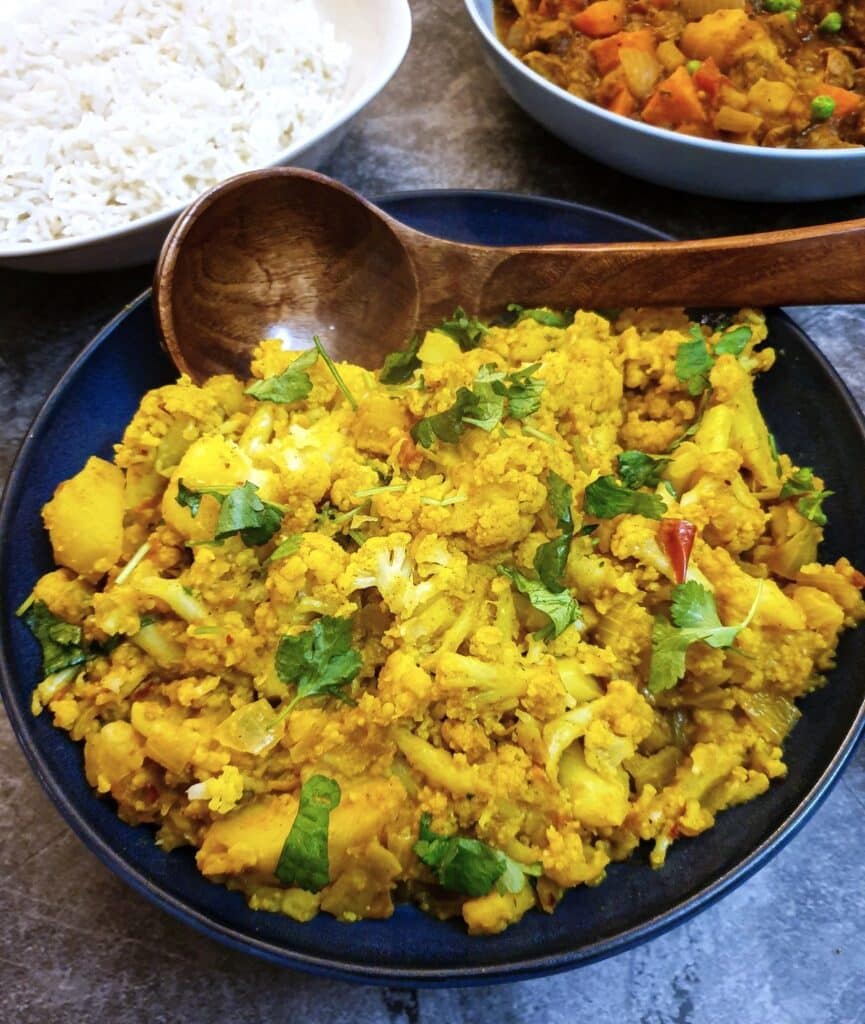 Aloo gobi in a serving dish with a wooden spoon.