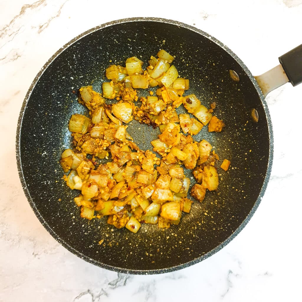 Onions and spices frying in a frying pan.