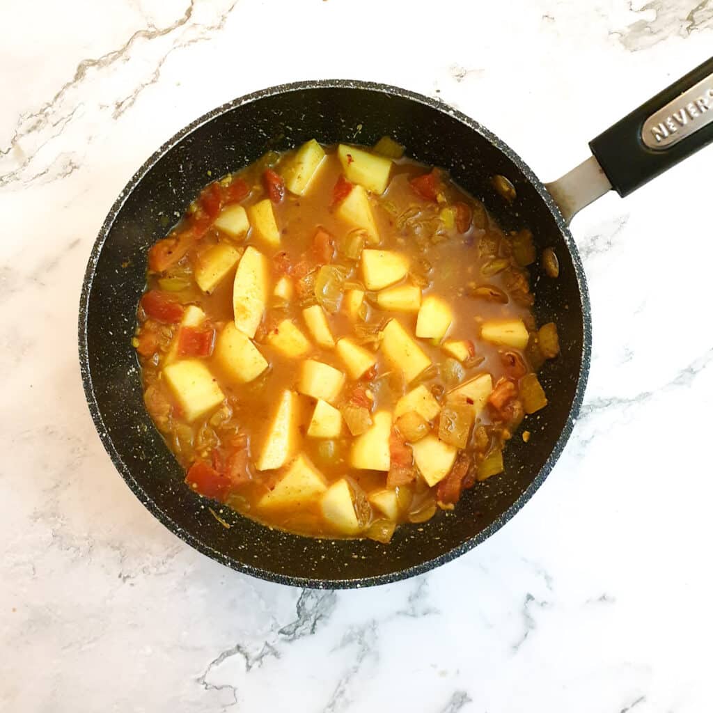 Potatoes and water added to the onions and tomatoes in the frying pan.