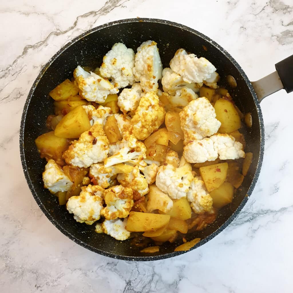 Cauliflower florets added to the aloo gobi in a frying pan.