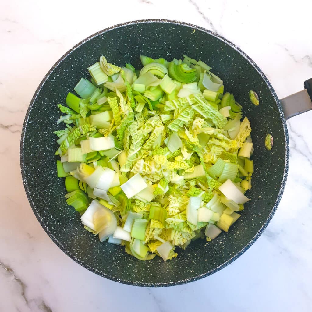 Raw sliced leeks and savoy cabbage in a saucepan.