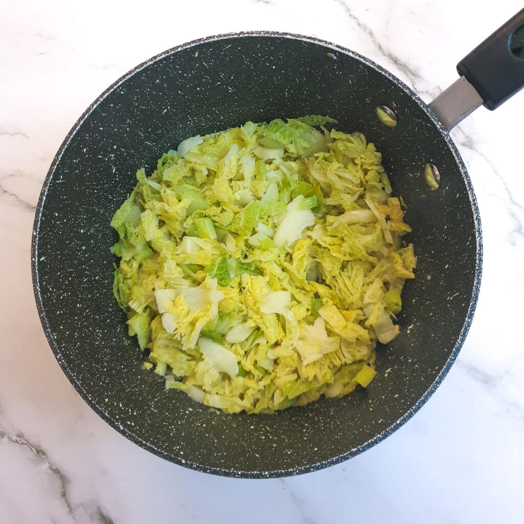 Cooked sliced leeks and savoy cabbage in a saucepan.