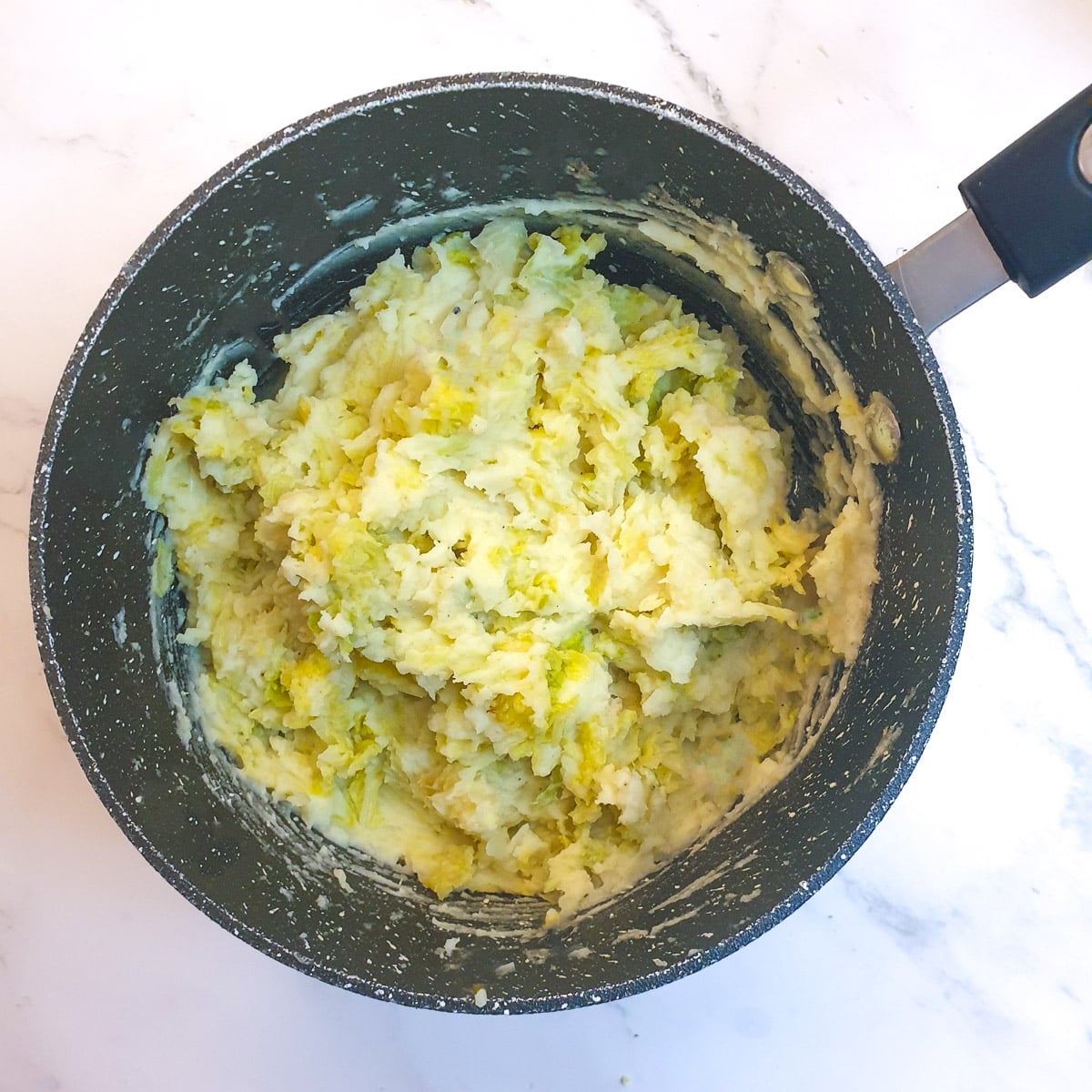 Cooked leeks and cabbage stirred into mashed potatoes in a saucepan.