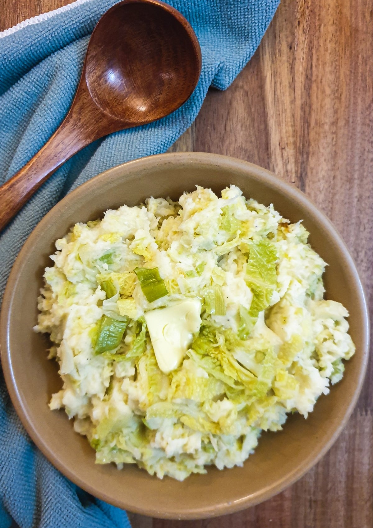 A dish of colcannon on a table next to a wooden serving spoon.