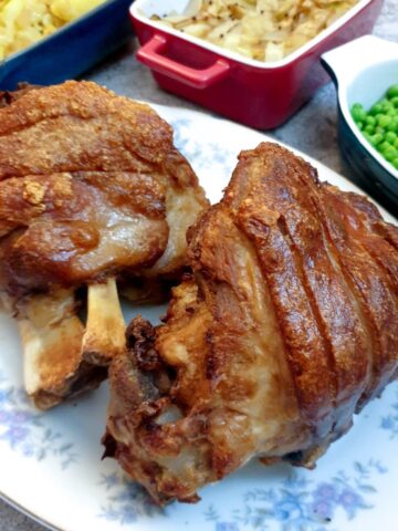 Two crispy-skinned eisbein on a plate next to a selection of vegetables.