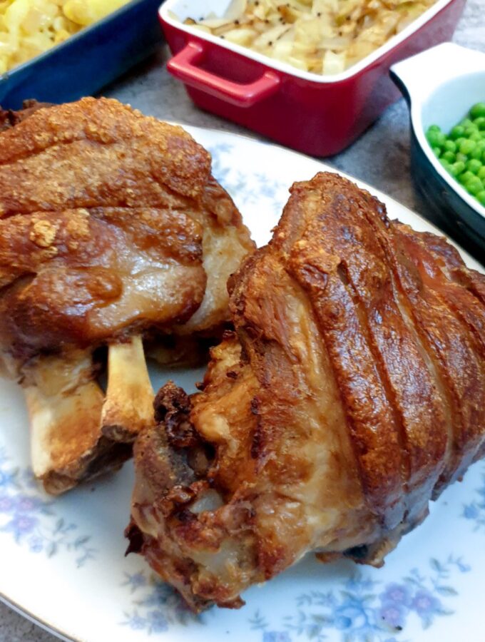 Two crispy-skinned eisbein on a plate next to a selection of vegetables.