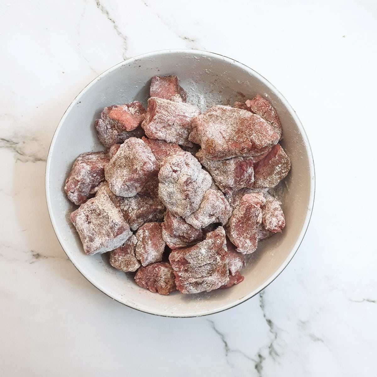 A bowl of cubed beef which has been coated with seasoned flour.