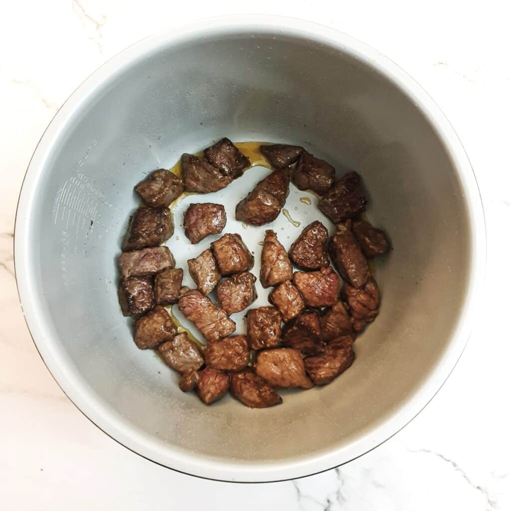 Cubes of beef browning in a pressure cooker.