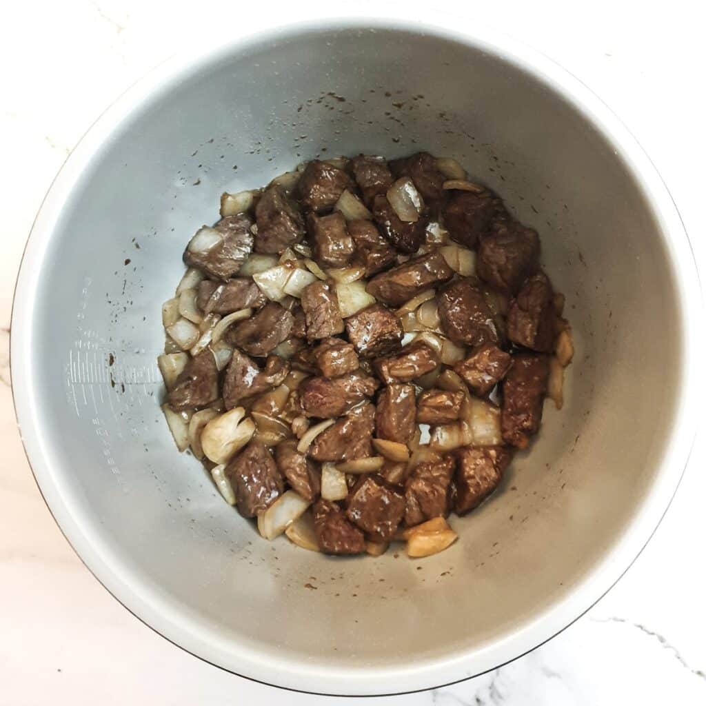Beef and onions browning in a pressure cooker.