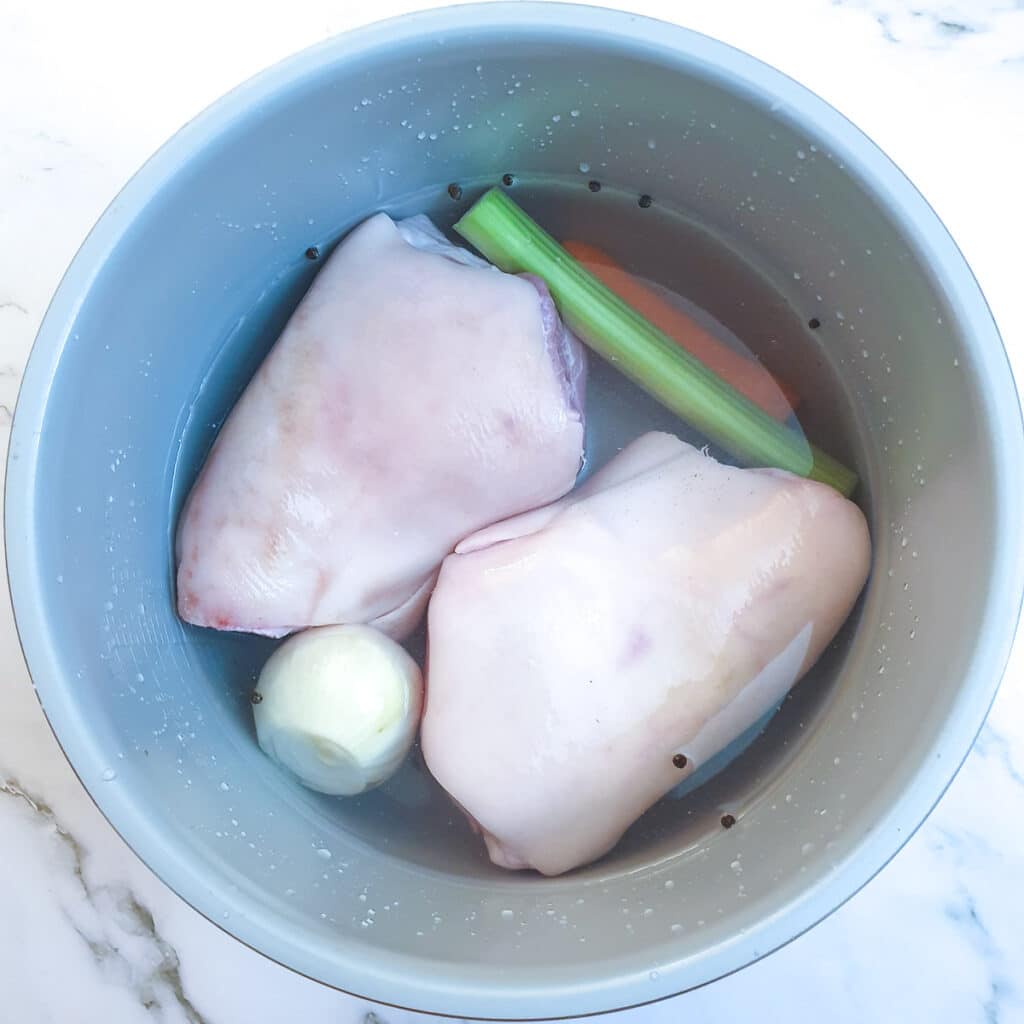 2 uncooked eisbein in a pressure cooker with celery, onions and carrots.