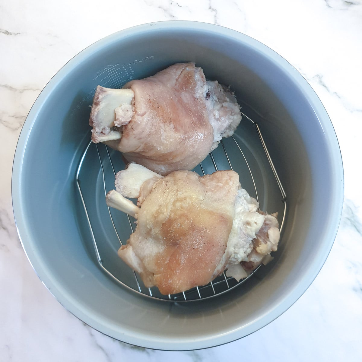 2 cooked eisbein on a try in the inner pot of a Ninja pressure cooker ready to be grilled.