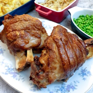 Two crispy-skinned eisbein on a plate next to a selection of vegetables.