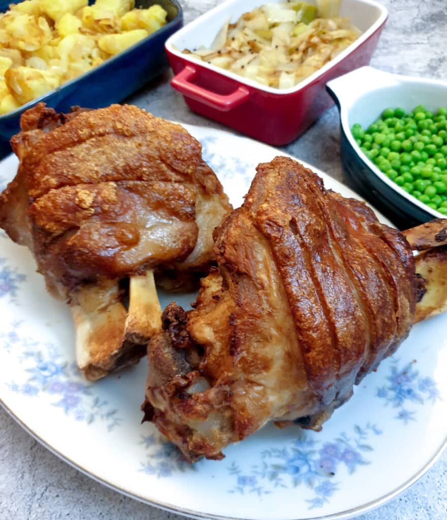 Two crispy-skinned eisbein on a plate next to a selection of vegetables.