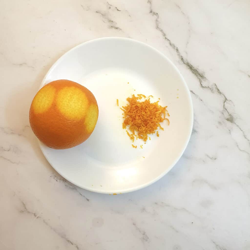 An orange on a place with orange zest.