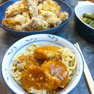 A dish of crispy chicken pieces on a bed of noodles, covered with orange sauce.