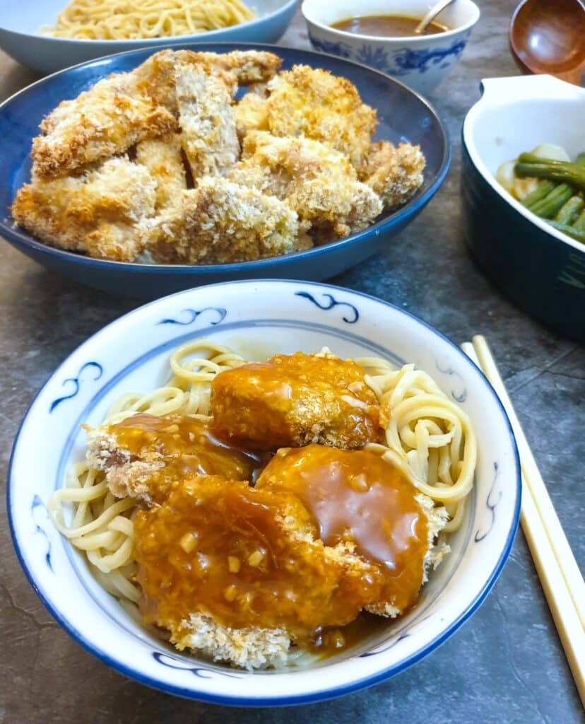 A dish of crispy chicken pieces on a bed of noodles, covered with orange sauce.
