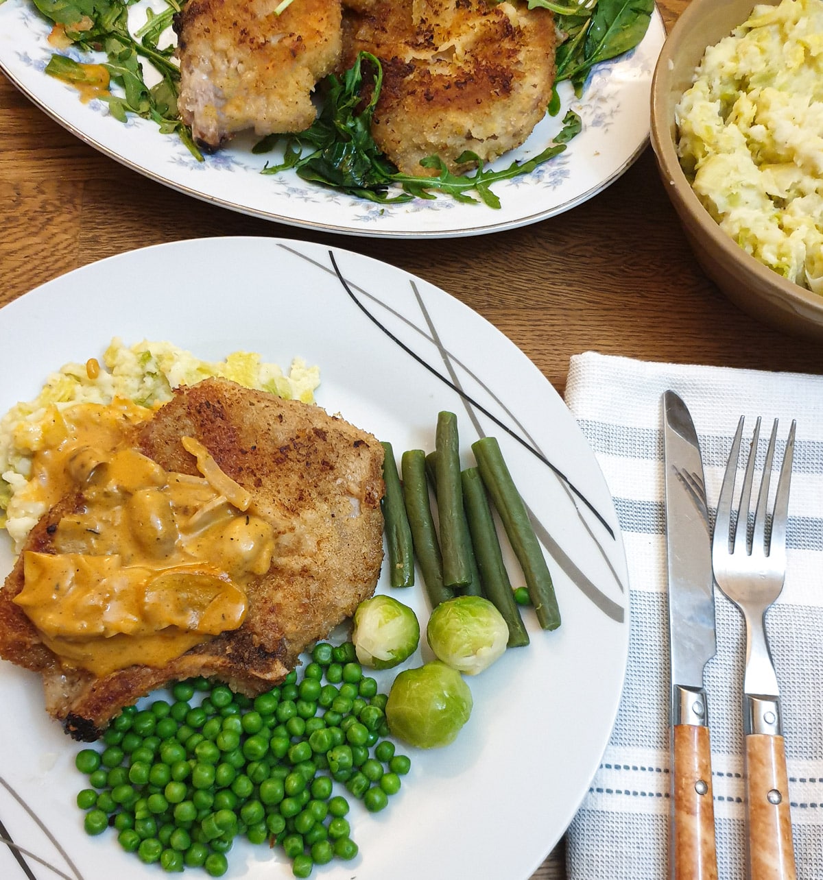 A pork chop on a plate with potatoes, vegetables and mushroom gravy.