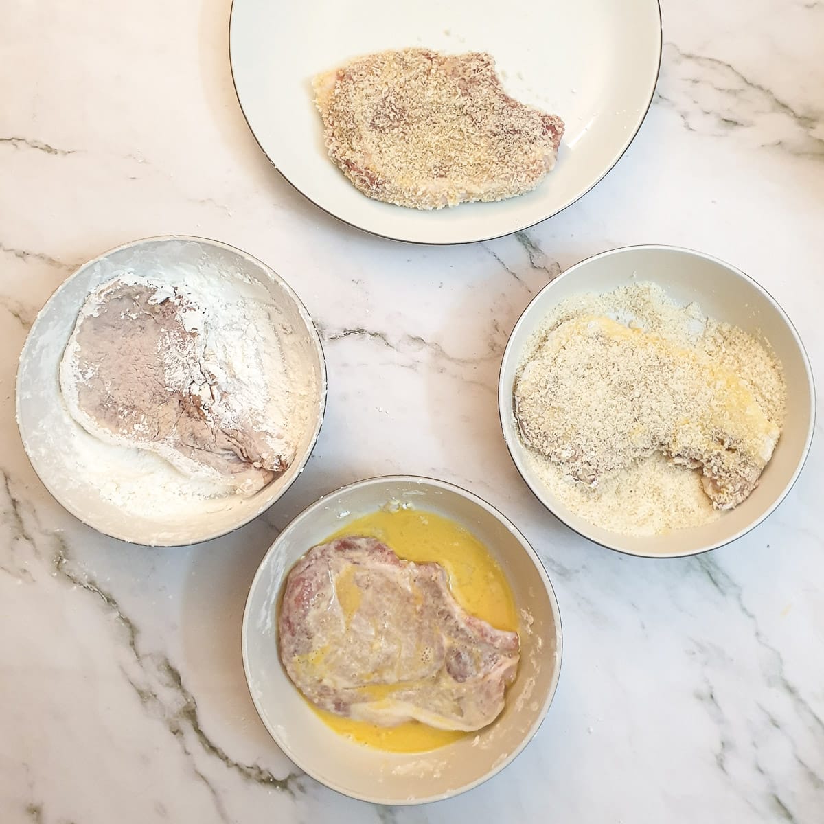 Pork chops being coated with cornflour, egg and breadcrumbs.